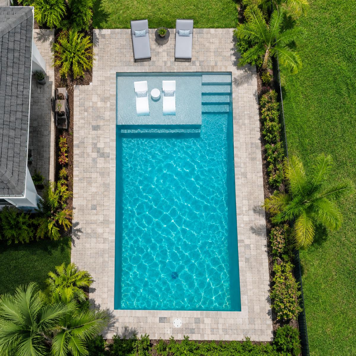 Aerial view of a rectangular pool with a tanning ledge and paver deck
